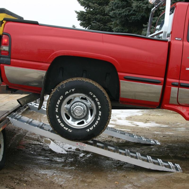 HD Ramps aluminum hook-end trailer ramps safely supporting a pickup truck actively loading onto the trailer.