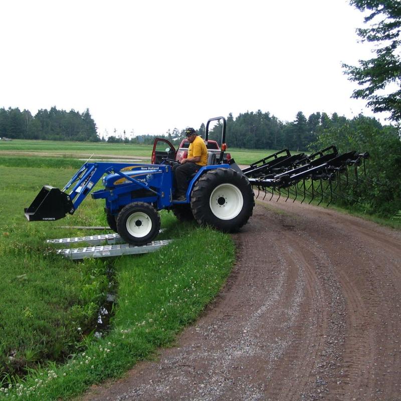HD Ramps aluminum plate-end ramp used as a sturdy bridge for a tractor crossing a small ditch.